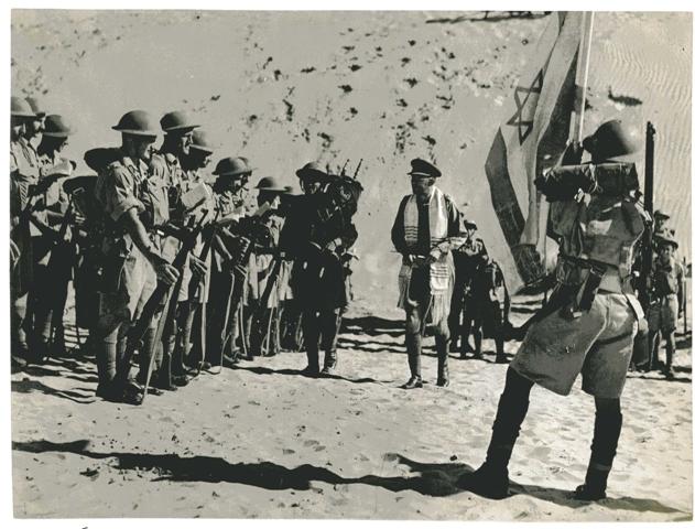 חייל מפלוגת מכבי נושא ספר תורה, עובר בין חיילי הפלוגה לפני צאתם לקרב מול האויב הנאצי